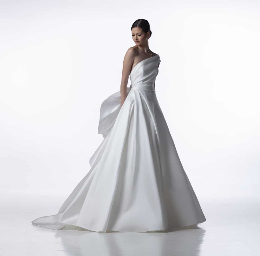 For the luxury bride who desires a wedding dress as bold and unforgettable as her love, the Valentini Spose Catera couture wedding gown emerges from the shadows. This one-shoulder masterpiece sculpts mikado silk into an architectural wonder, designed to make you feel like a modern goddess on your wedding day. Find your dream wedding dress at your Dream Bridal near Boston.