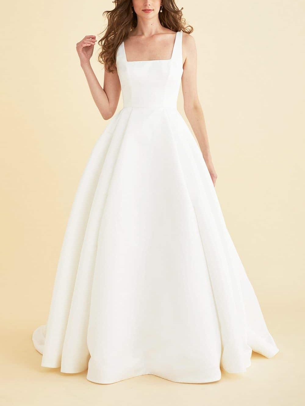 Lea-Ann Belter Astral eco-duchess satin wedding dress features a square neckline and draped back bow. Pleated for polished volume, the skirt with pockets sails into a chapel train. Find your dream wedding dress at Your Dream Bridal near Boston.