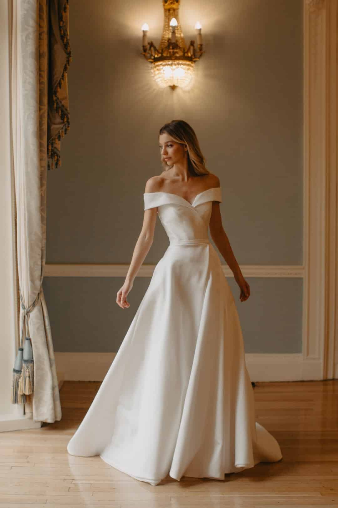 Beautifully structured in silk Mikado, the Suzanne Neville Allegri off the shoulder wedding dress has a fabulous full skirt with pockets! Find your wedding dress at Your Dream Bridal in Sudbury MA.