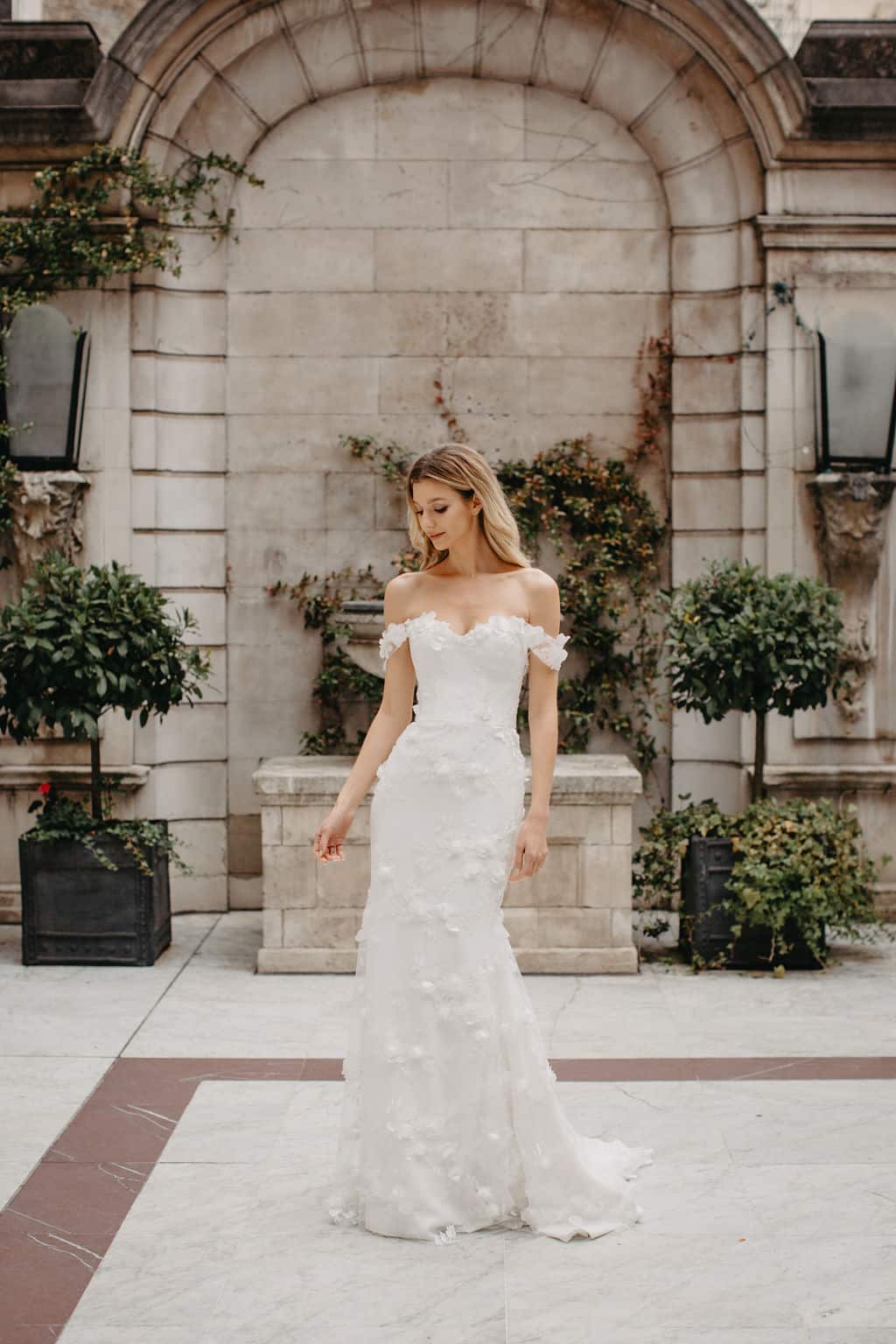 Dreamy Suzanne Neville Debussy wedding gown has a corseted cupped bodice with off the shoulder floral straps and a fitted skirt in our pretty Debussy floral tulle. Find your wedding dress at Your Dream Bridal in near Boston.